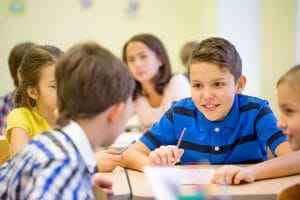 Education, elementary school, learning and people concept - group of school kids talking during lesson in classroom