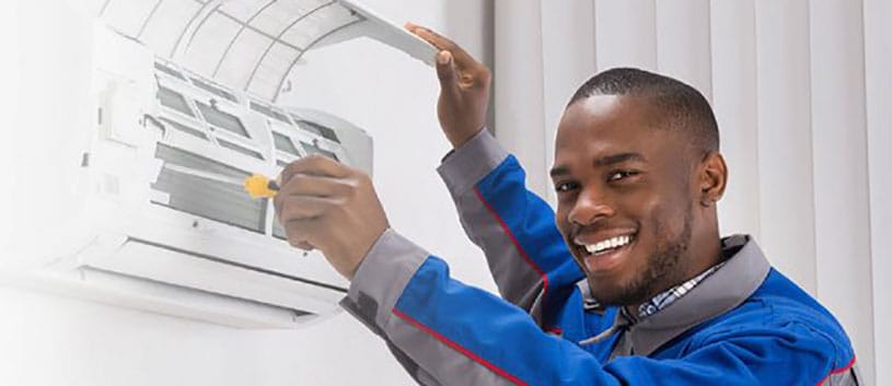 An IntelliTec College Refrigeration and HVAC student is working on an air conditioner and smiling for the camera